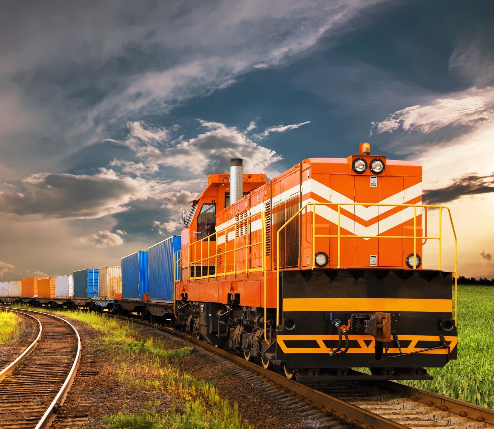 Orange freight train on curved tracks under a cloudy sky.